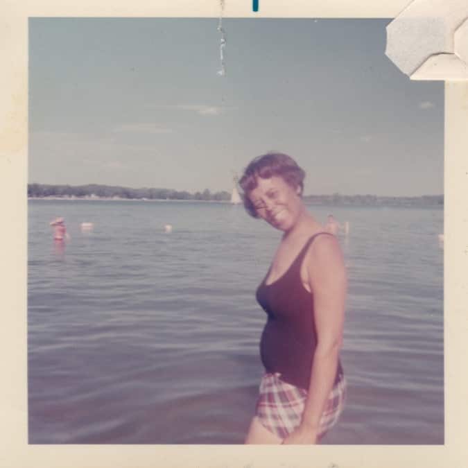 a woman stands and smiles by a lake
