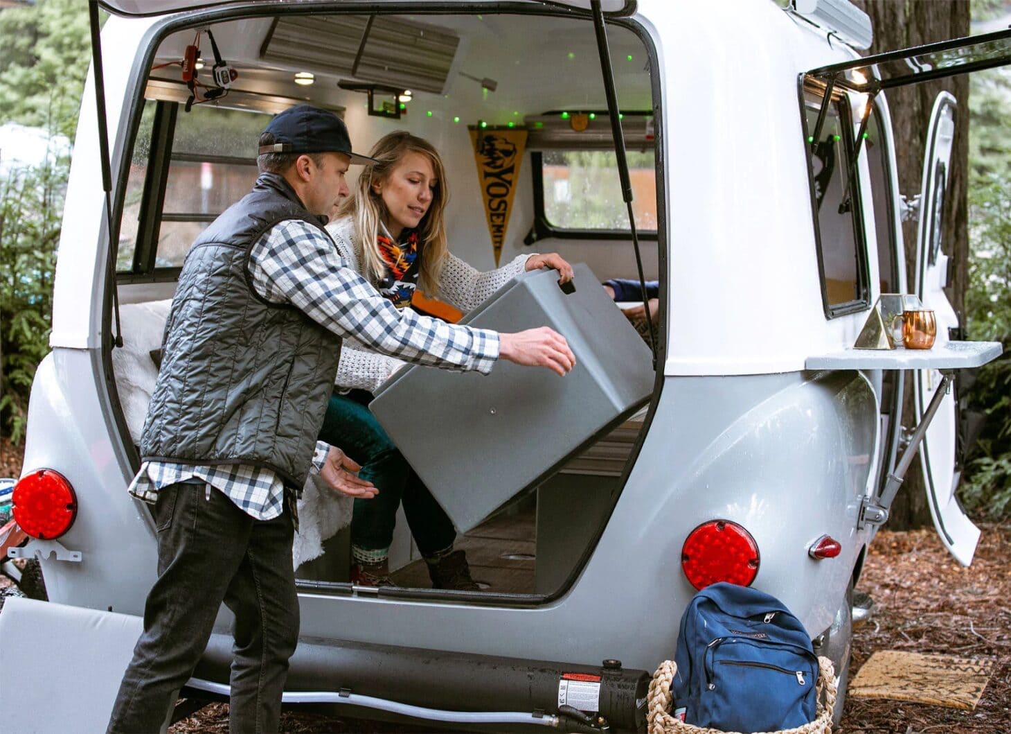 A couple loads gear into the hatchback opening in a small, trendy travel trailer RV.