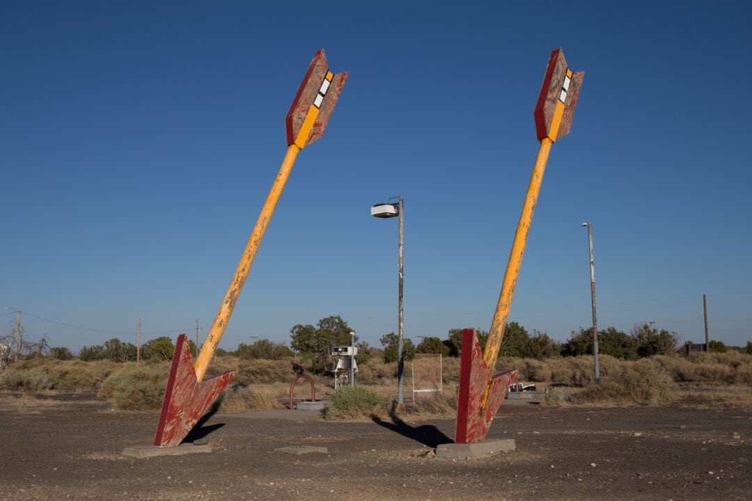 two large wooden arrows painted red and yellow stuck in the ground against a clear blue sky, flagstaff, arizona