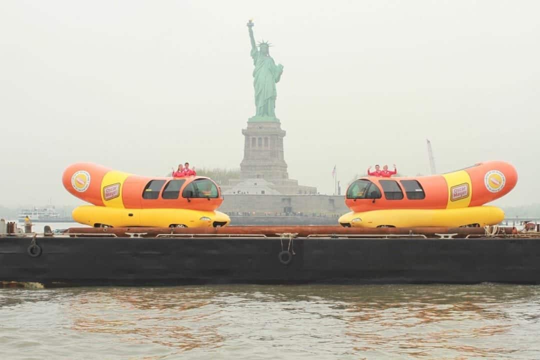 two wienermobiles in front of the statue of liberty on a barge